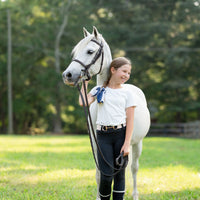 Little Girt standing next to a white horse in a grassy field with trees in the background
