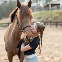 Girl kissing a horse in an outdoor arena