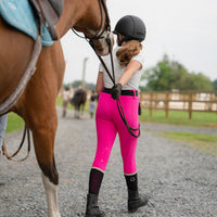 Person in pink riding legging breeches leadinng horse on a gravel path at barn