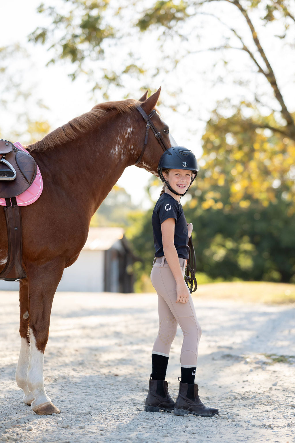 Girl in black equestrian shirt and tan leggings holding horse