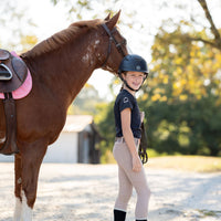Girl in black equestrian shirt and tan leggings holding horse