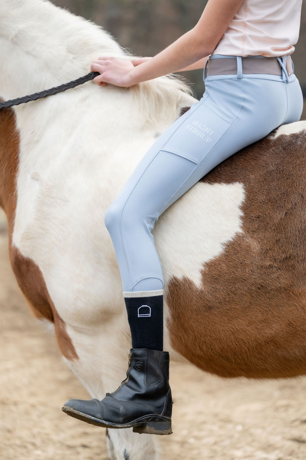Little Girl riding a horse wearing light blue riding pants leggings and short stirrup socks and belt