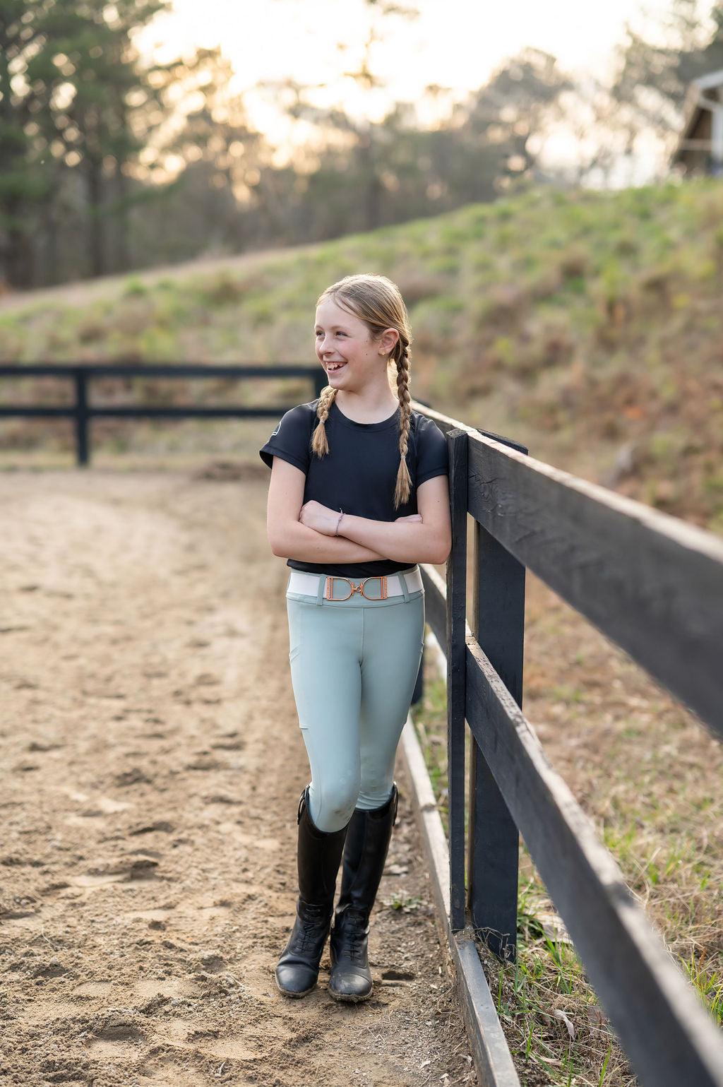 Girl standing by a fence in equestrian clothing