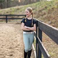 Girl standing by a fence in equestrian clothing