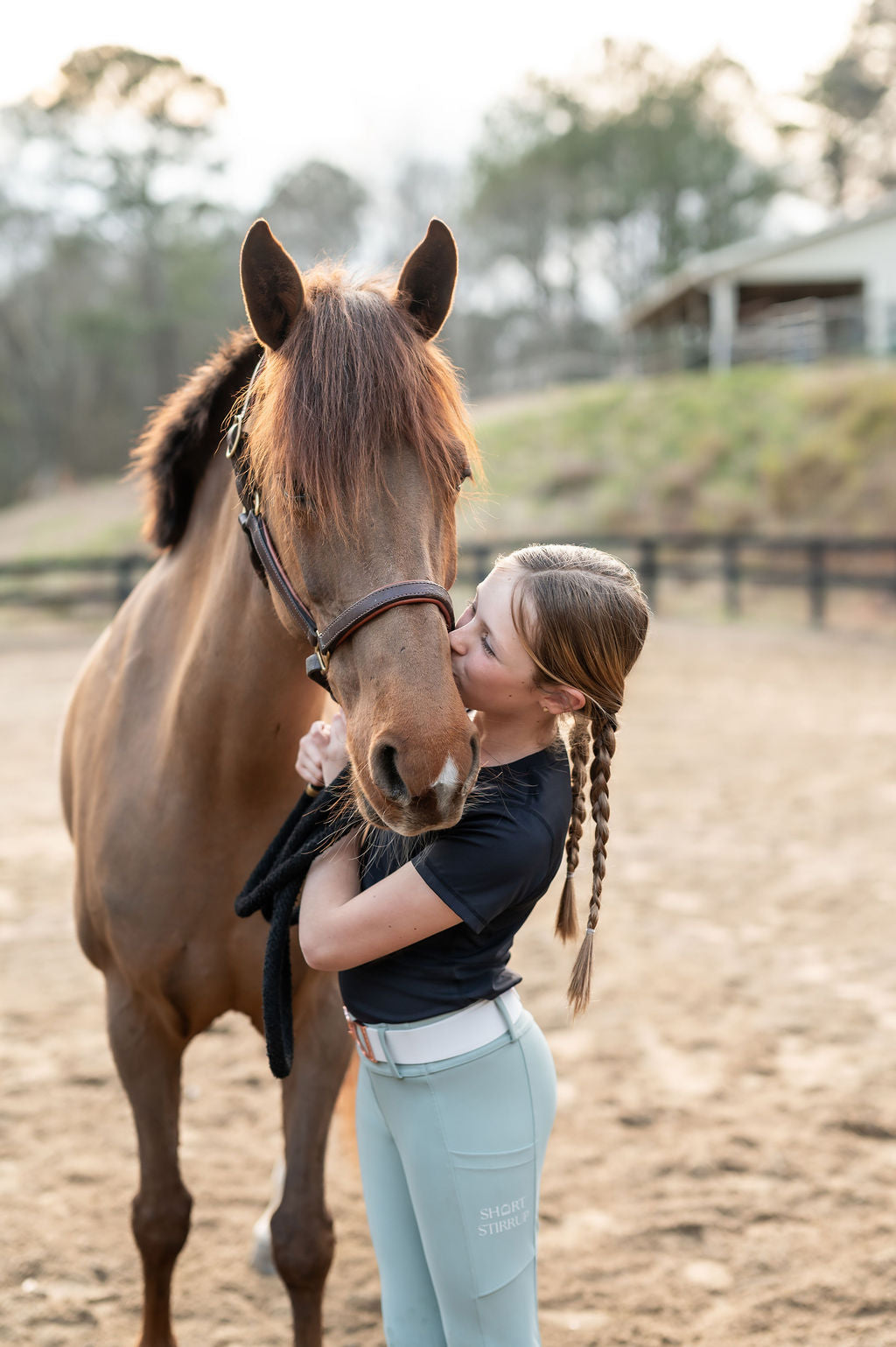 Girl kissing a horse in an outdoor arena