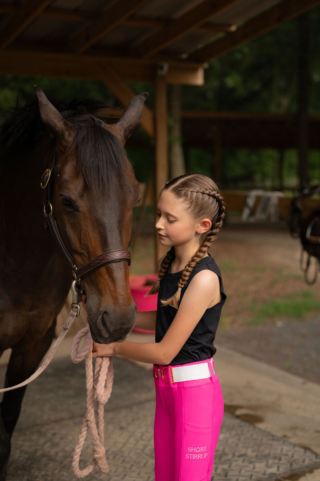 Young girl petting a horse in an outdoor stable in hot pink riding leggings jods breeches