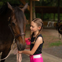 Young girl petting a horse in an outdoor stable in hot pink riding leggings jods breeches